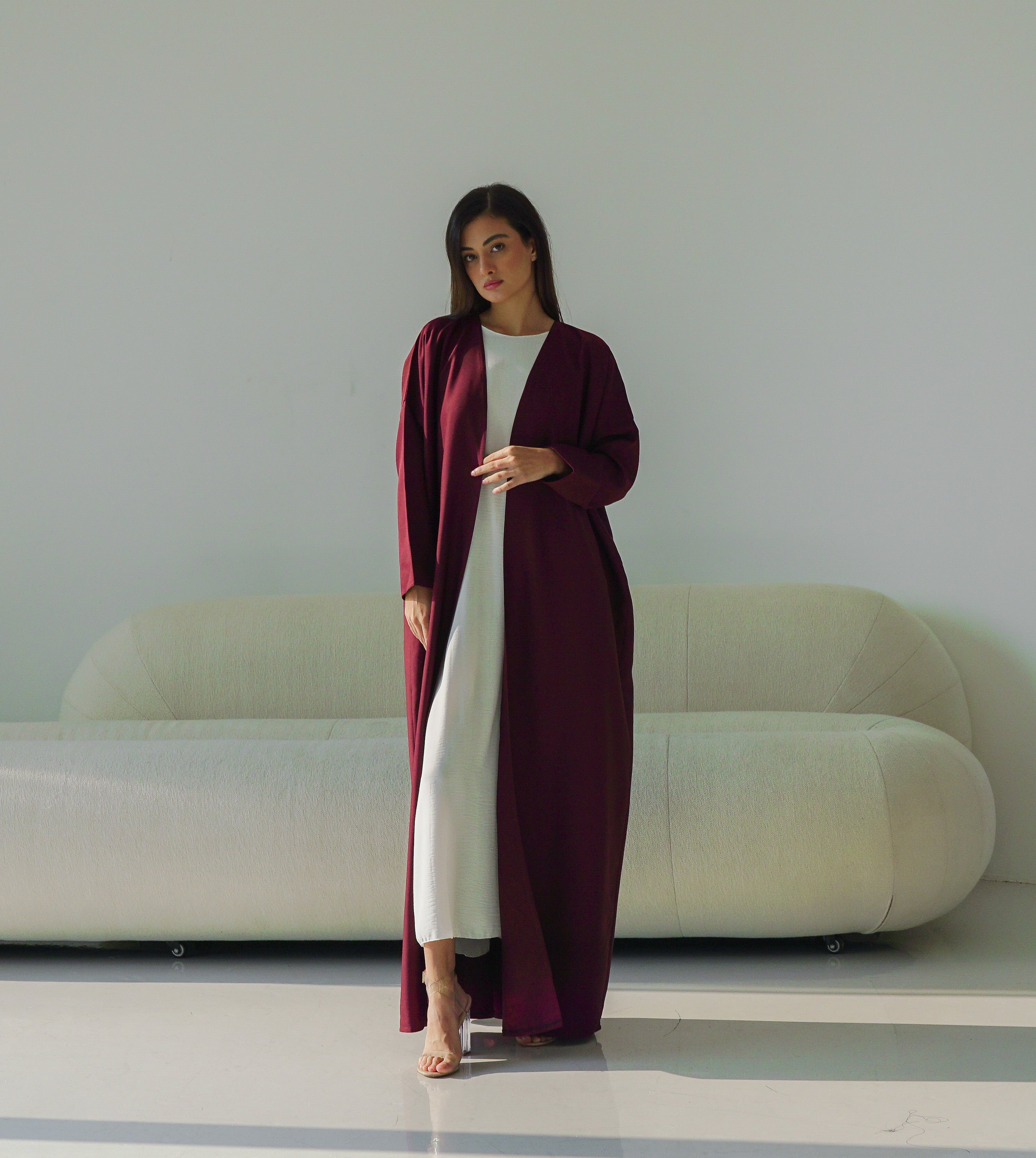 Woman in a long burgundy dress standing in a modern room with a white sofa.