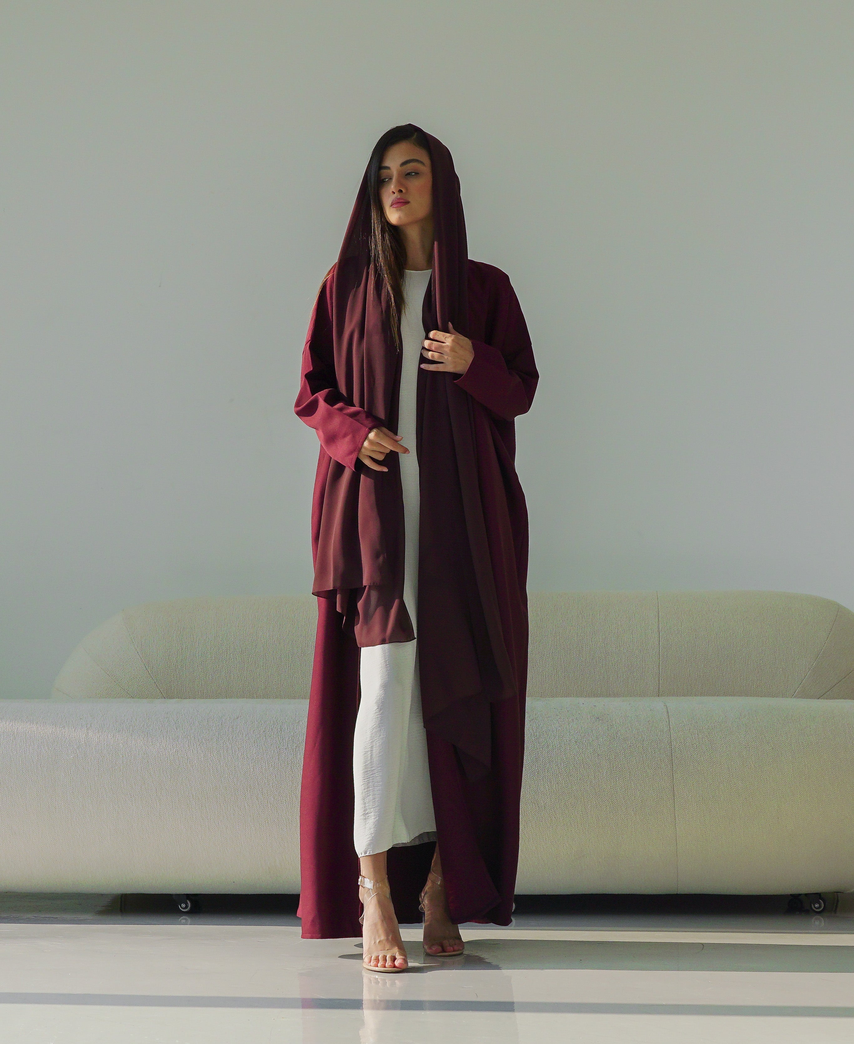 Woman in a long burgundy robe standing in a modern room with a white sofa and decorative vase.