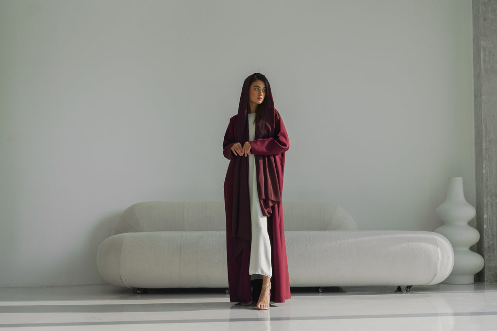 Woman in a long burgundy coat standing in a minimalistic room with a white sofa.